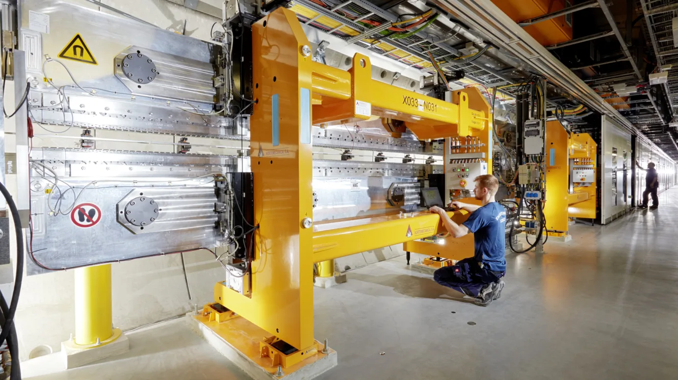 Un technicien travaille sur une grande machine jaune dans une installation technique dotée de câbles et de commandes