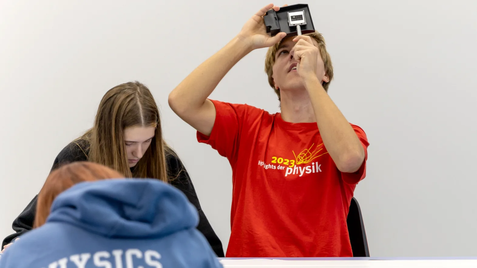Un jeune observe un objet scientifique avec un appareil, tandis que d’autres travaillent à une table