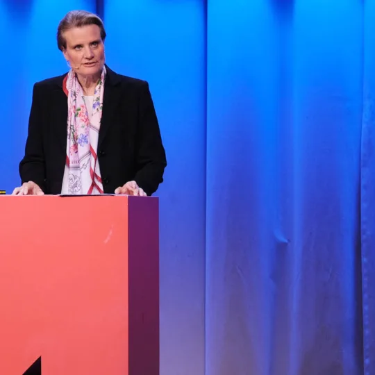 Une femme fait un discours à un pupitre en forme de flèche rouge.