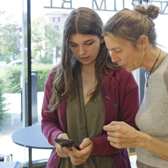 Zwei Frauen die gemeinsam auf ein Handy schauen.