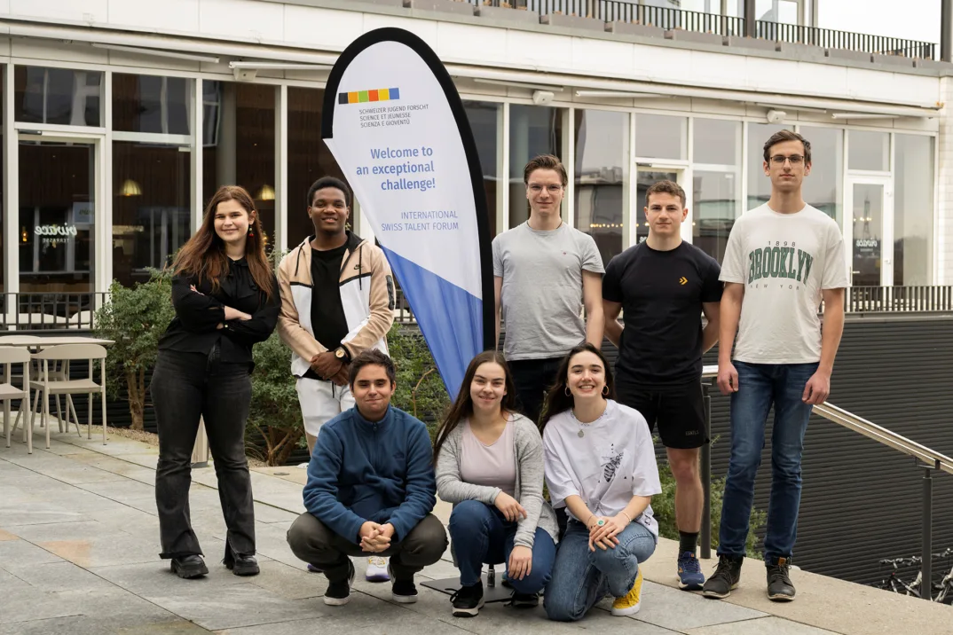 Gruppenbild mit sechs jungen Erwachsenen vor einer Fahne