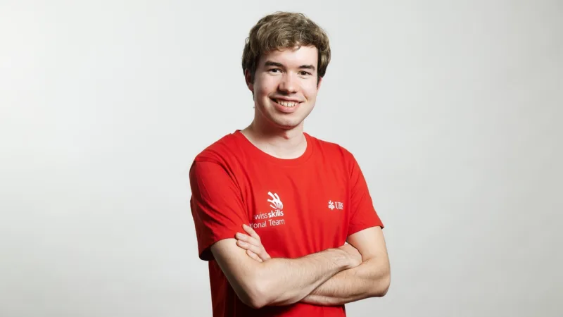 A man in a red T-shirt with his arms crossed, smiling