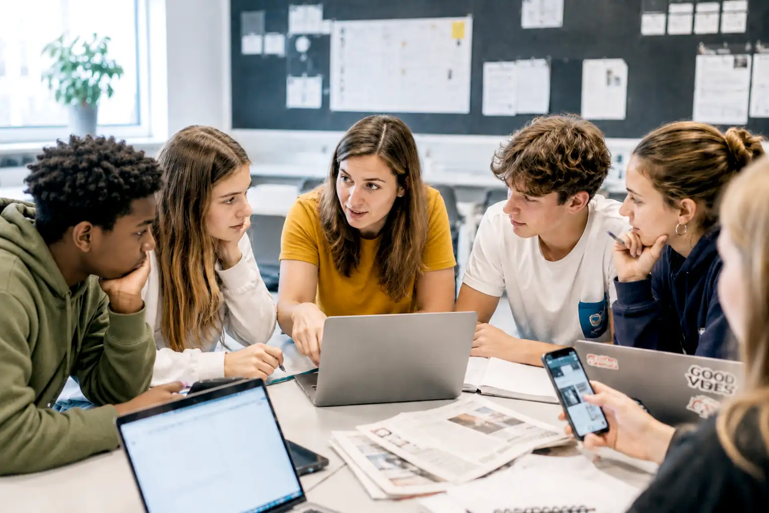 Gruppe von jungen Menschen sitzen im Halbkreis an einem Tisch, diskutierend, Laptops und Papier auf dem Tisch